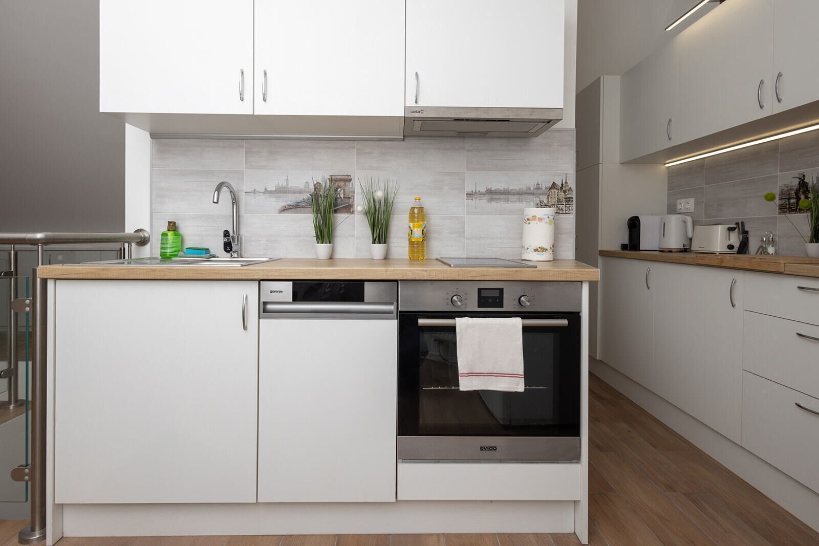 Una cocina moderna con armarios blancos, horno empotrado y lavavajillas de acero inoxidable.