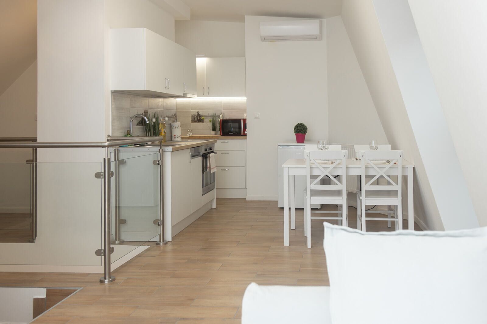 Eine moderne Küche mit weißen Schränken, einem Kühlschrank mit Glastür sowie einem Essbereich mit weißen Stühlen und einem Tisch.