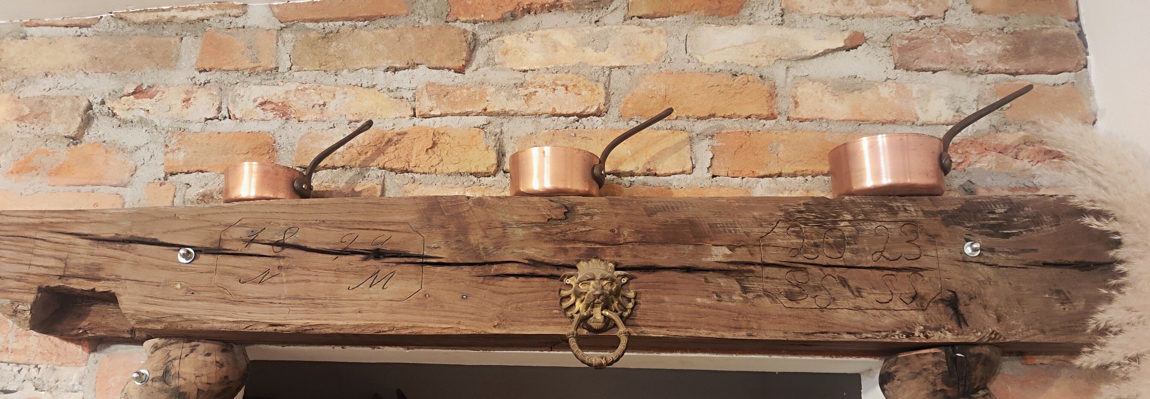 Une cheminée rustique ornée de trois pots en cuivre posés sur une étagère en bois.