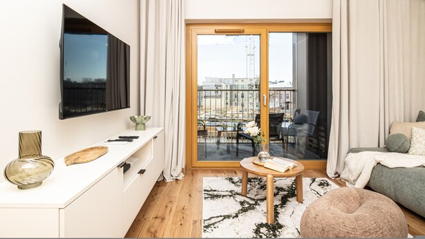 Un soggiorno moderno con una TV a schermo piatto, una zona pranzo con tavolo e sedie, e un balcone con vista sulla città.