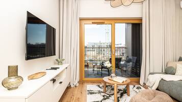 A modern living room with a flat-screen TV, a dining area with a table and chairs, and a balcony with a view of the city.