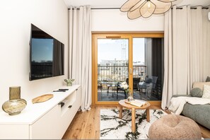 A modern living room with a flat-screen TV, a dining area with a table and chairs, and a balcony with a view of the city. - Venecia Apartament Balkon Nowy Port Bydgoszcz (Bydgoszcz)