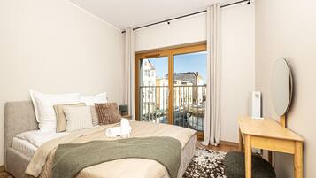 A hotel room with a bed, a bedside table, a mirror, and a view of buildings through a large window.