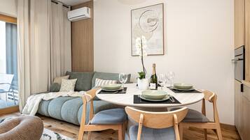 A modern living room with a dining area, featuring a sofa, a table set for two, and a mounted air conditioner.
