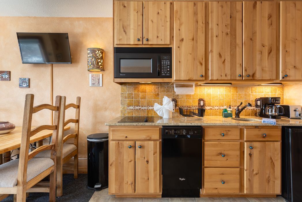 A kitchen with wooden cabinets, a microwave, a dishwasher, and a tiled backsplash.