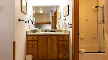 A bathroom with wooden cabinets, a sink, a mirror, and a glass-enclosed shower.