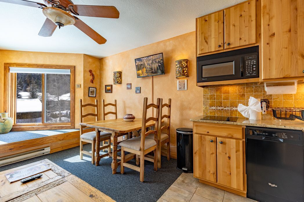 A kitchen with wooden cabinets, a microwave, a dishwasher, and a dining area with chairs and a table.