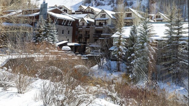 Un xalet cobert de neu amb diversos edificis, incloent una xemenea destacada, envoltat d'arbres i un paisatge nevós.