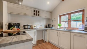 A modern kitchen with white cabinets, a built-in oven, and a large window. - Waterside Cottage in Pancrasweek (Holsworthy)