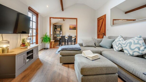A modern living room with a sofa, a television, and a dining area in the background. - Waterside Cottage in Pancrasweek (Holsworthy)