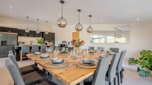 A modern dining area with a wooden table set for six, surrounded by grey upholstered chairs. - Weekstone Waterside Barn (Holsworthy)
