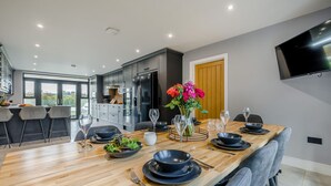 Une cuisine moderne avec des meubles de couleur sombre, une table à manger en bois pour six personnes et une grande fenêtre donnant sur un jardin.