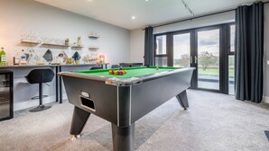 Une table de billard dans une pièce dotée d’une grande fenêtre, d’un coin bar et offrant une vue sur l’extérieur.