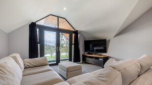 Un salon moderne doté d’un grand canapé d’angle, d’un téléviseur à écran plat et d’une porte-fenêtre coulissante donnant sur un balcon avec vue sur la verdure.