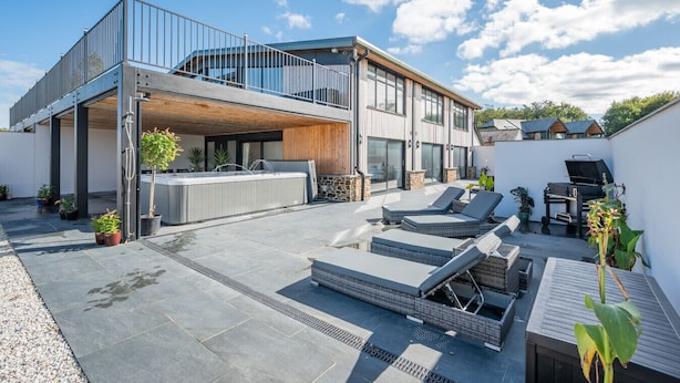 Une maison moderne à deux étages dotée d’un patio couvert, d’un espace salon extérieur et d’un coin barbecue.