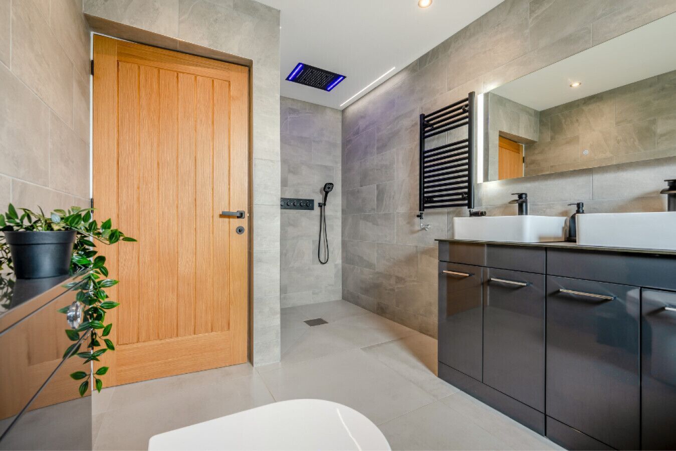 Une salle de bain moderne avec une porte en bois, un espace douche, un grand miroir et un lavabo doté d’un robinet noir.