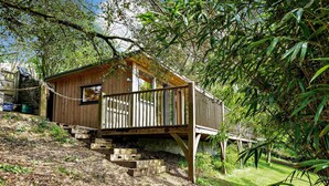 Een houten chalet met een houten terras, omringd door dichte beplanting en een stenen trap die erheen leidt.