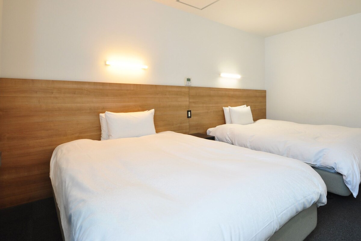 Ein Hotelzimmer mit zwei Betten, einem Holzkopfteil und Wandleuchten.