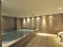 Un moderno cuarto de spa con una amplia bañera de hidromasaje rectangular, paredes con azulejos e iluminación empotrada.