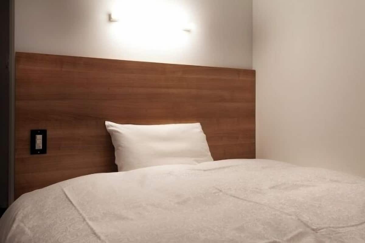 A bed with a wooden headboard, a white pillow, and a wall-mounted light fixture.