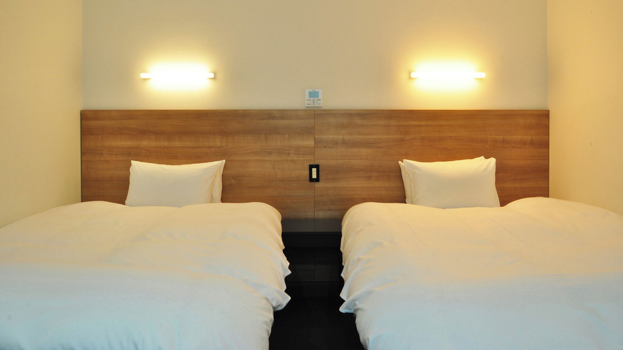 Ein Hotelzimmer mit zwei Betten, einem Holzkopfteil, Wandleuchten und einem kleinen Nachttisch.