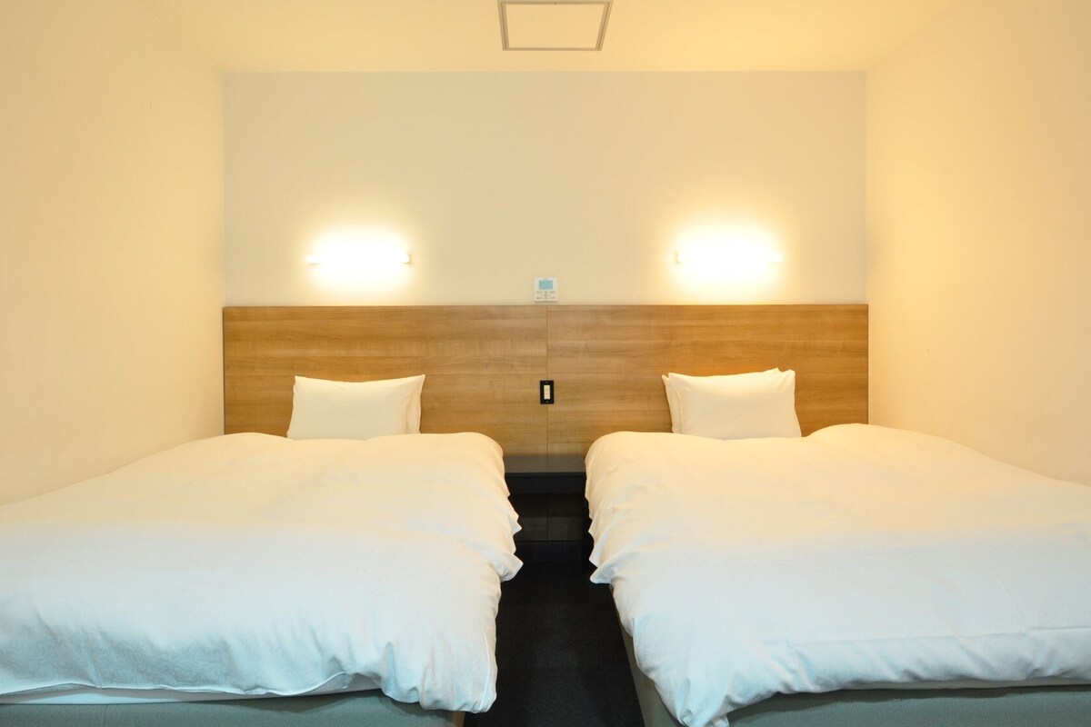 Ein Hotelzimmer mit zwei Einzelbetten, einem Holzkopfteil und zwei Wandleuchten.