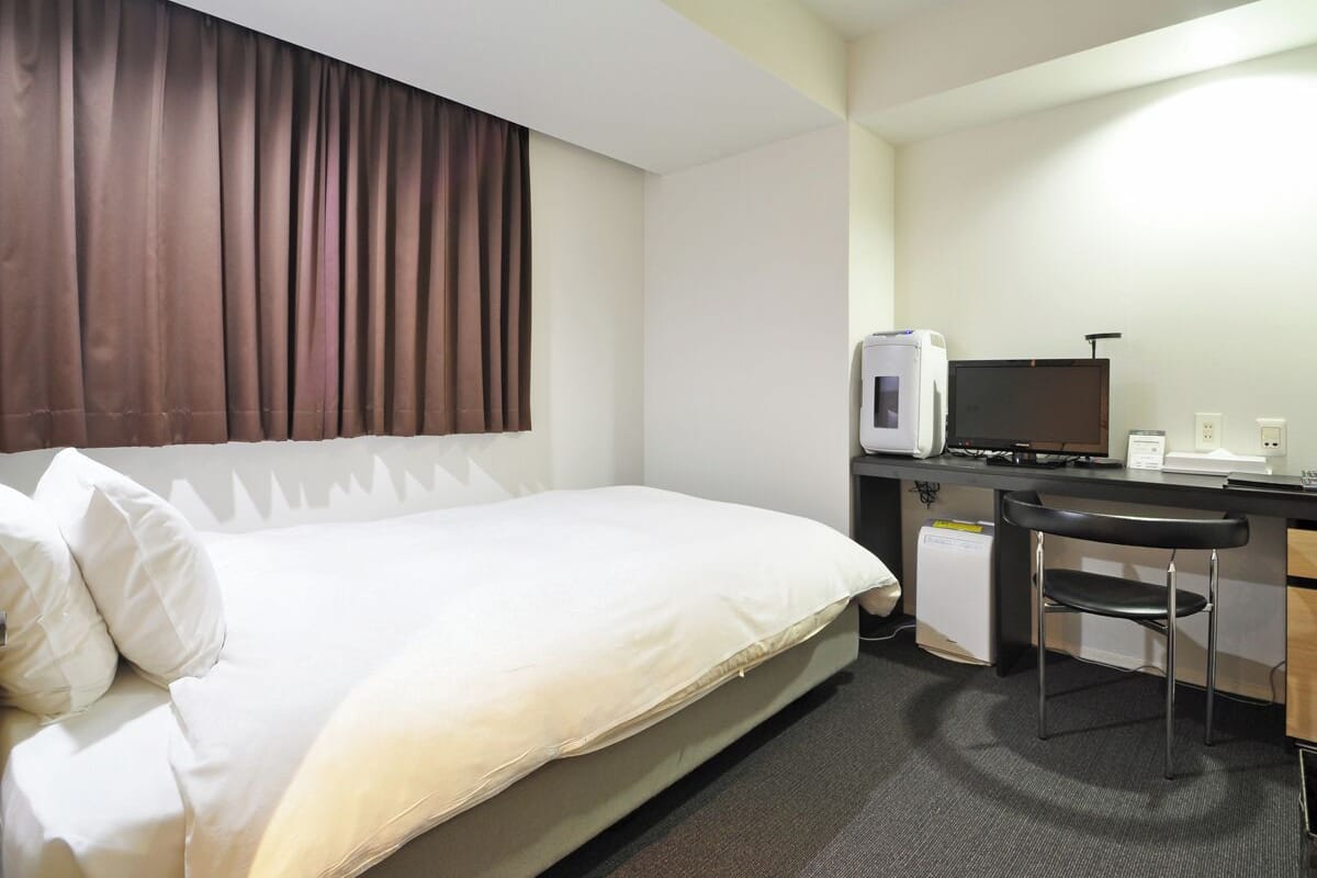 A hotel room with a bed, a desk with a computer, a TV, and a microwave.