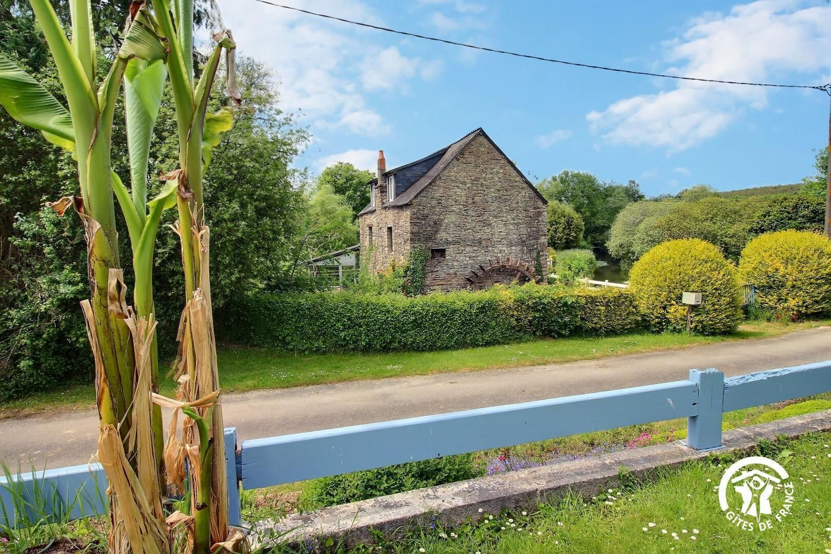 Un bâtiment en pierre à l’architecture traditionnelle, entouré d’une végétation luxuriante et sous un ciel dégagé.