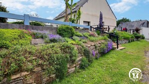 Ein Haus mit geneigtem Dach, einer Steinsichtmauer und verschiedenen Pflanzen und Blumen.