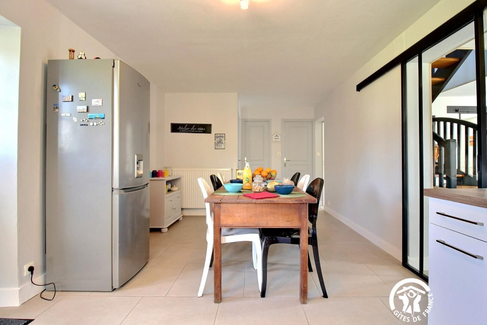 A modern kitchen with a refrigerator, a dining table with chairs, and a window overlooking a staircase.