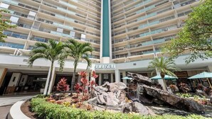 Un hotel de gran altura con varios balcones, un atrio central y un área exterior ajardinada con rocas y plantas.