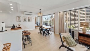 Una sala de estar moderna con comedor, ventanas amplias con vistas a la ciudad y un paisaje urbano visible a través de las ventanas.