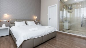Un dormitorio moderno con una cama grande, mesitas de noche, cabina de ducha de vidrio y pared con estampado.