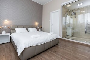 Ein modernes Schlafzimmer mit einem großen Bett, Nachttischen, einer Duschkabine aus Glas und einer Wand mit Muster.