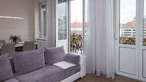 Una sala de estar moderna con un sofá gris, una mesa de comedor con sillas y un balcón con barandilla de metal.