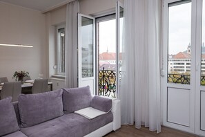Ein modernes Wohnzimmer mit einem grauen Sofa, einem Esstisch mit Stühlen und einem Balkon mit Metallgeländer.