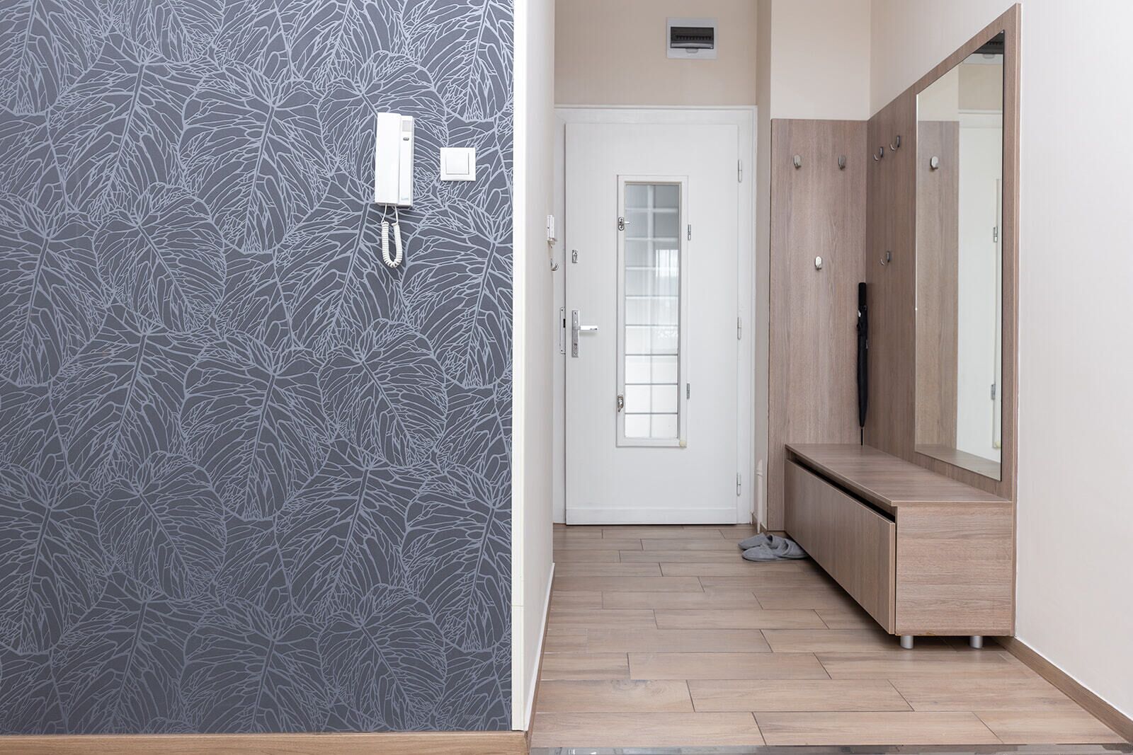 A hallway with a patterned wall, a white door with a frosted glass panel, a wooden bench, and a large mirror.