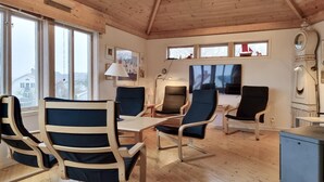 A cozy room with wooden floors, a large window, and a TV. There are four chairs and a table. - Awesome home in Fiskebäckskil with house sea view (Fiskebäckskil)