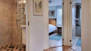 A bathroom with a shower, a sink, and a toilet. There is a bed with a window and a lamp in the adjacent room. - Awesome home in Fiskebäckskil with house sea view (Fiskebäckskil)