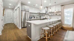 A modern kitchen with white cabinetry, stainless steel appliances, and a central island with bar stools. - Sleeps 14 | Bikes | Sunshine State of Mind | 30A | Pool | Beach Access (Inlet Beach)