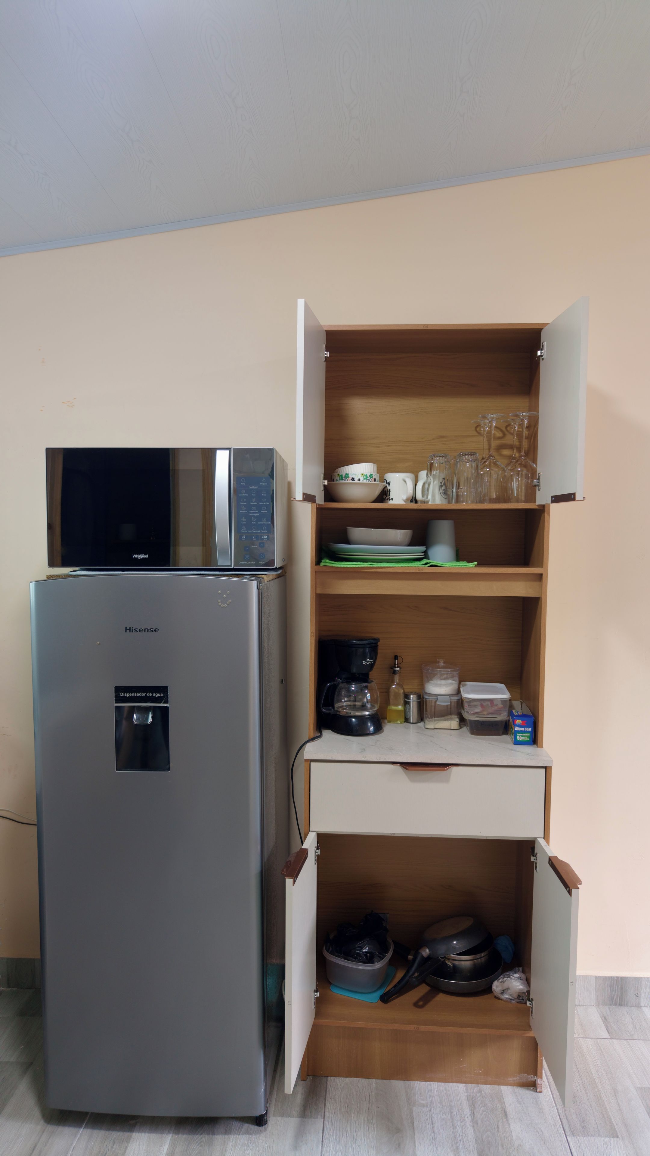 Une cuisine compacte équipée d’un réfrigérateur Hisense, d’un four à micro-ondes et d’un meuble en bois doté d’étagères où sont rangés les ustensiles de cuisine.