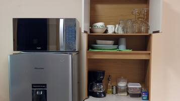 Une cuisine compacte équipée d’un réfrigérateur Hisense, d’un four à micro-ondes et d’un meuble en bois doté d’étagères où sont rangés les ustensiles de cuisine.