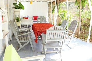 A covered outdoor seating area with white furniture and a red tablecloth.
