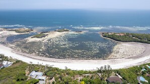 Vista aérea de una zona costera con playa, formaciones rocosas y edificios dispersos.