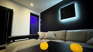 Une chambre d’hôtel moderne avec un mur de couleur sombre, un canapé de couleur claire et deux lampes jaunes posées sur une table en bois.