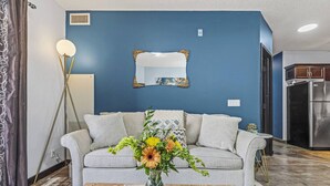 A living room with a grey sofa, a vase with flowers, a floor lamp, and a kitchen in the background. - Perfect Rockies Escape with Pool, Hot Tub and Gym (Canmore)