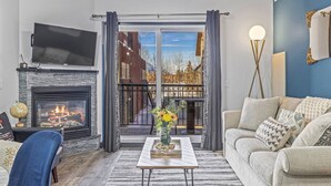 A living room with a fireplace, a sofa, a coffee table, and a view of a snowy outdoor area through a glass door. - Perfect Rockies Escape with Pool, Hot Tub and Gym (Canmore)