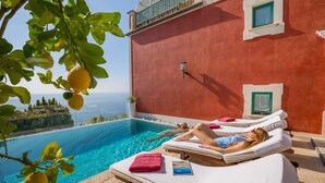 Zona junto a la piscina con dos sillones reclinables, un edificio rojo y vista al mar.