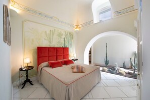 Ein geräumiges Schlafzimmer mit einem großen Bett, einem roten Kopfteil und Blick auf eine Wüstenlandschaft durch einen Bogen.