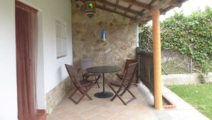 Un patio con pared de piedra, una mesa con sillas, un farol y techo de madera.